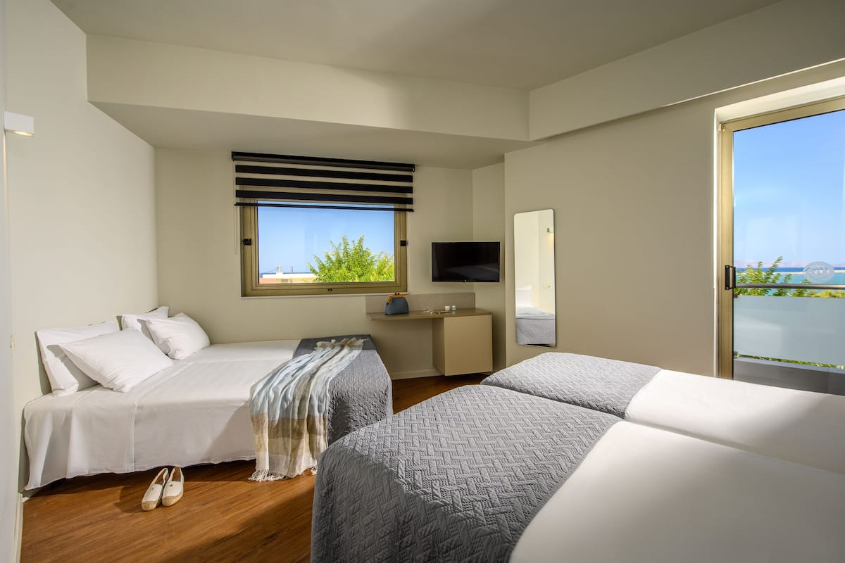 A hotel room with two beds, a TV, a small desk, and a window with a view.