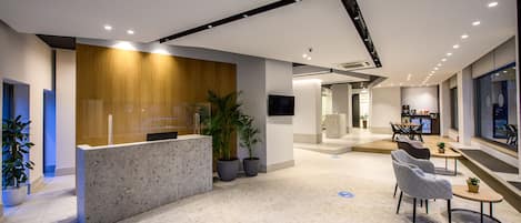 A modern reception area with a marble counter, potted plants, and seating.