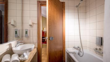 Une salle de bain avec une porte en bois, un lavabo blanc, un miroir, une douche et un porte-serviettes.