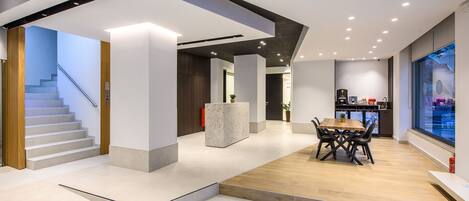 A modern interior with a staircase, a central seating area, and a kitchen visible through a glass wall.