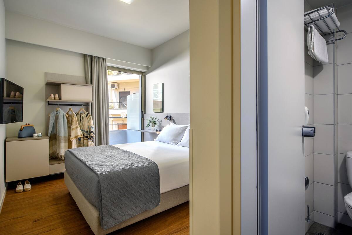 A hotel room with a bed, a wardrobe, a bathroom, and a view of the outside balcony.