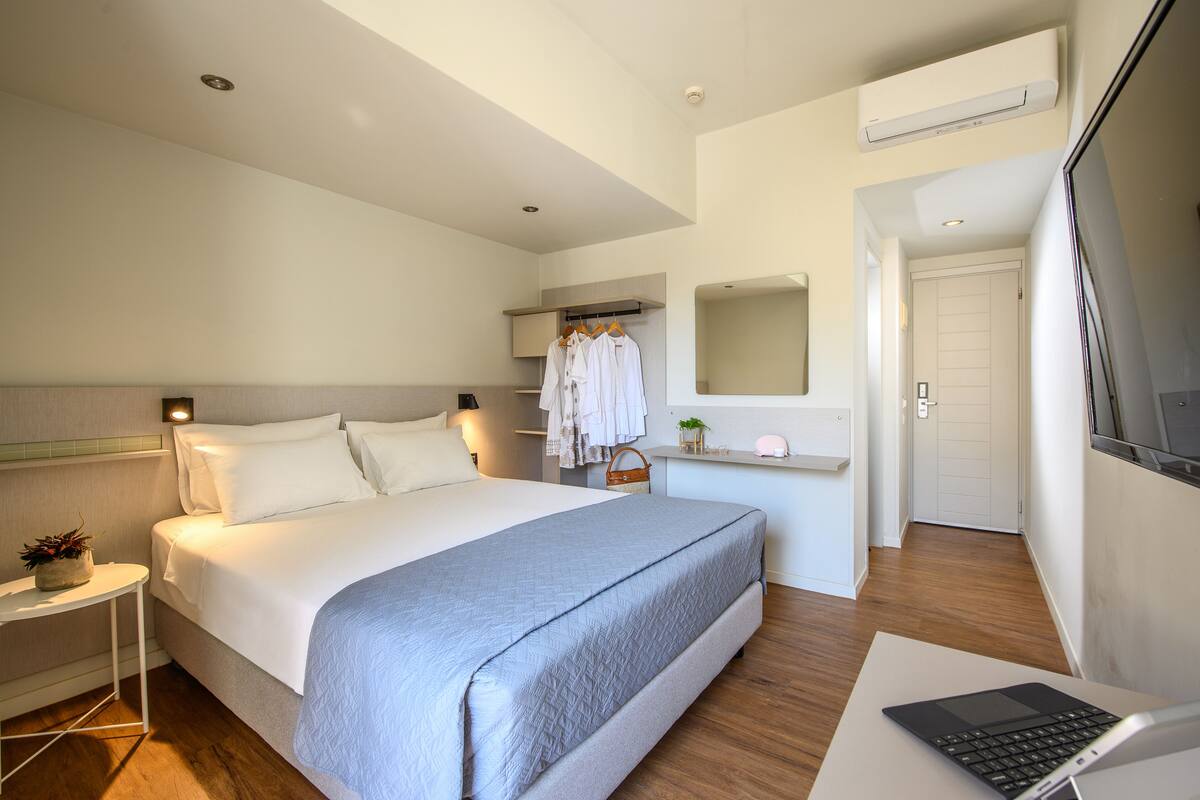 A modern hotel room with a large bed, bedside table, and a laptop on a desk.