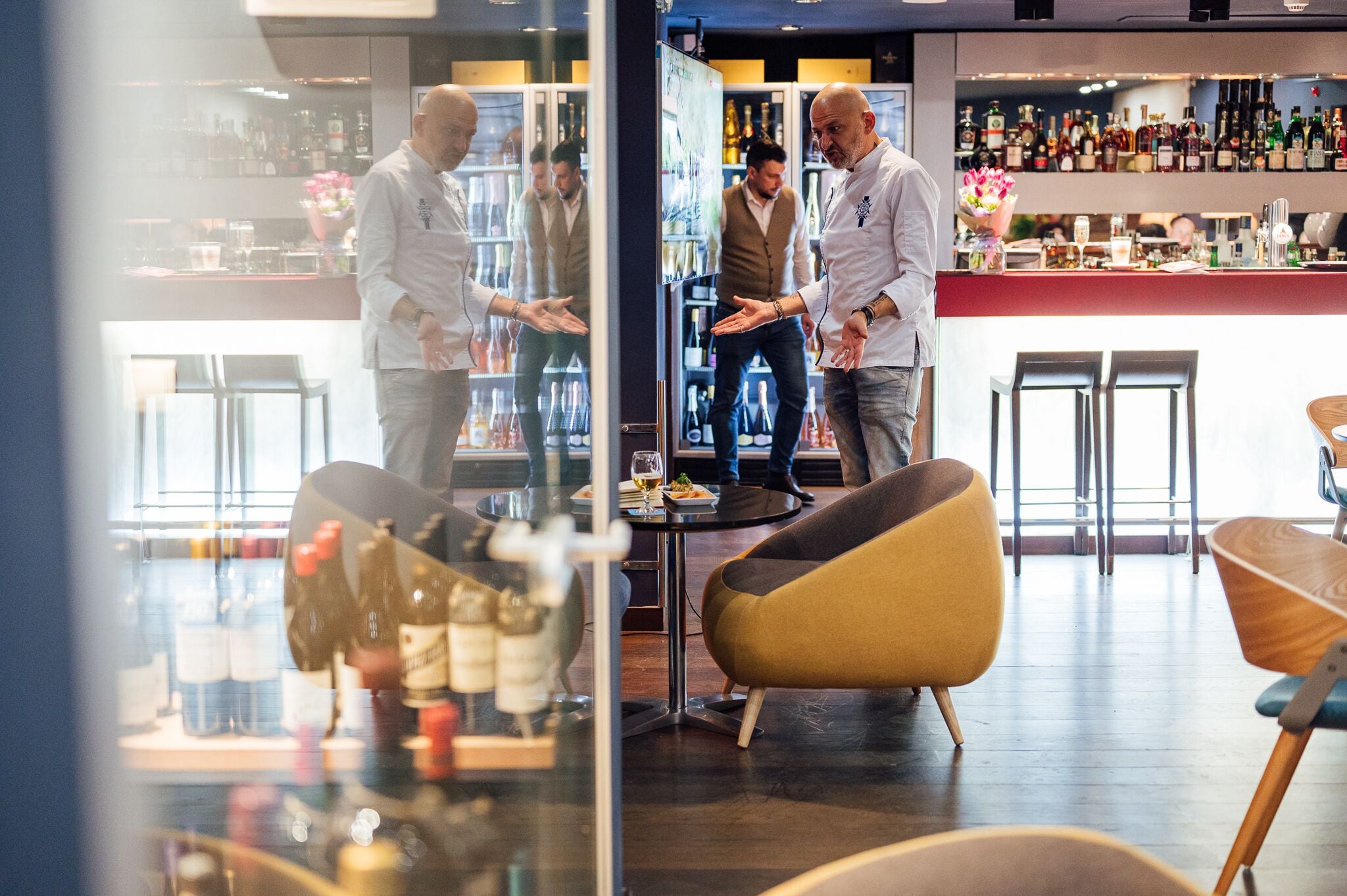A modern bar area with a glass partition, a round table, and bar stools.