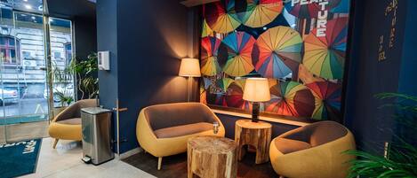 A modern lobby with two yellow armchairs, a wooden stool, and a wall mural with colorful umbrellas.