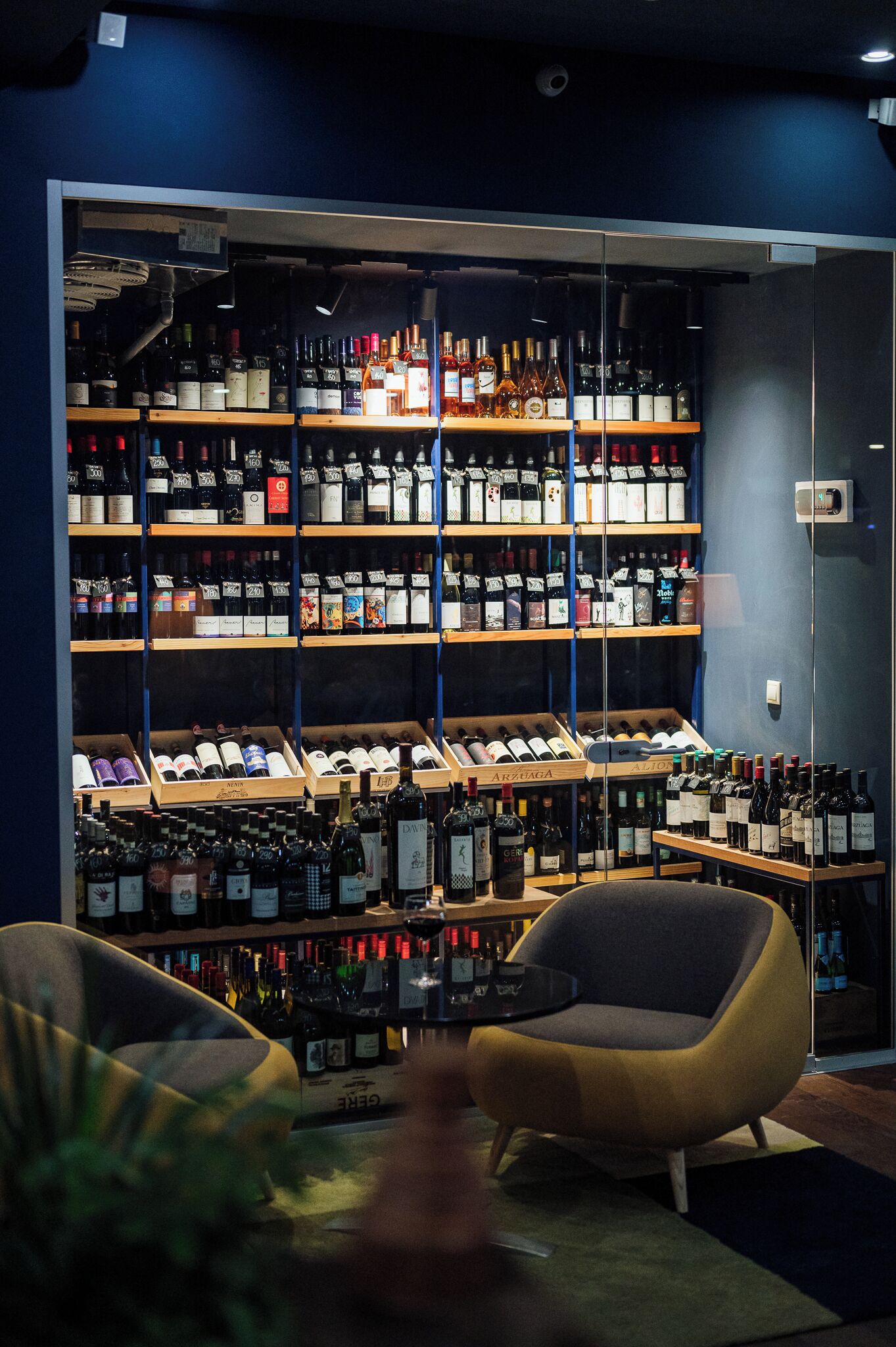 Uma adega com prateleiras cheias de garrafas de vinho, um bar com balcão e duas cadeiras.