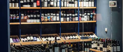 Uma adega com prateleiras cheias de garrafas de vinho, um bar com balcão e duas cadeiras.
