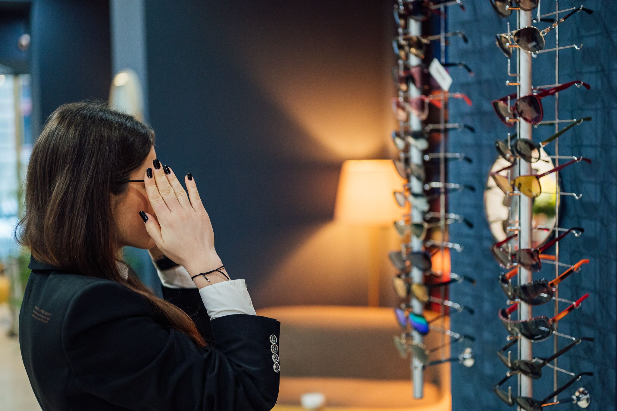 A person examining eyeglasses in a store with a display of various frames.