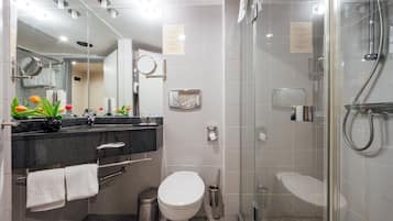 Ein modernes Badezimmer mit einer Duschkabine, einer Toilette und einem Waschbecken mit Spiegel und Handtuchhalter.