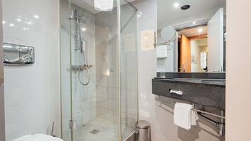 Un baño moderno con ducha envuelta en vidrio, inodoro blanco, encimera de granito y un espejo.