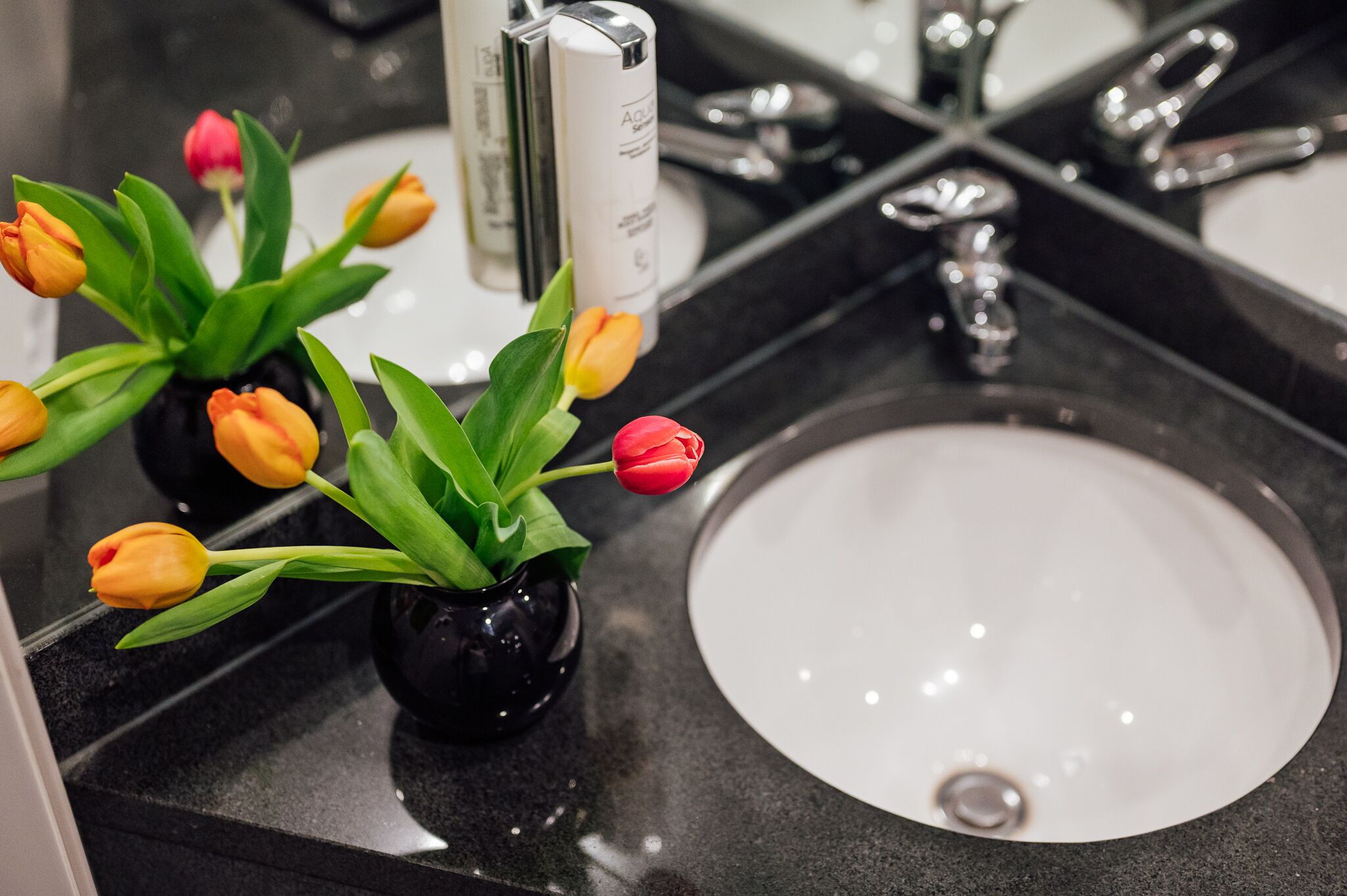 A bathroom sink with a black countertop and a vase of tulips.