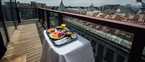 A balcony with breakfast setup including fruits, eggs, and juice, overlooking a cityscape with historic buildings.
