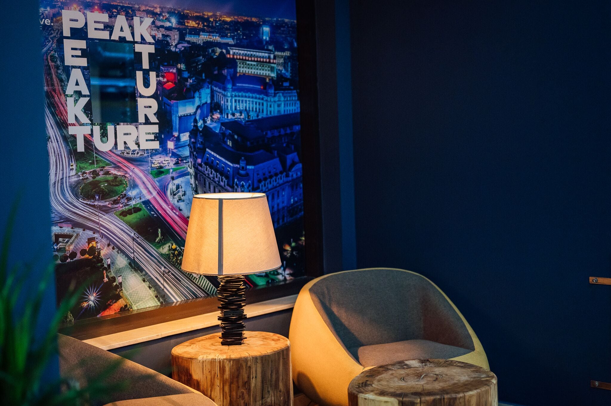 A modern room with a cityscape poster, a lamp on a wooden stump, and a curved chair.