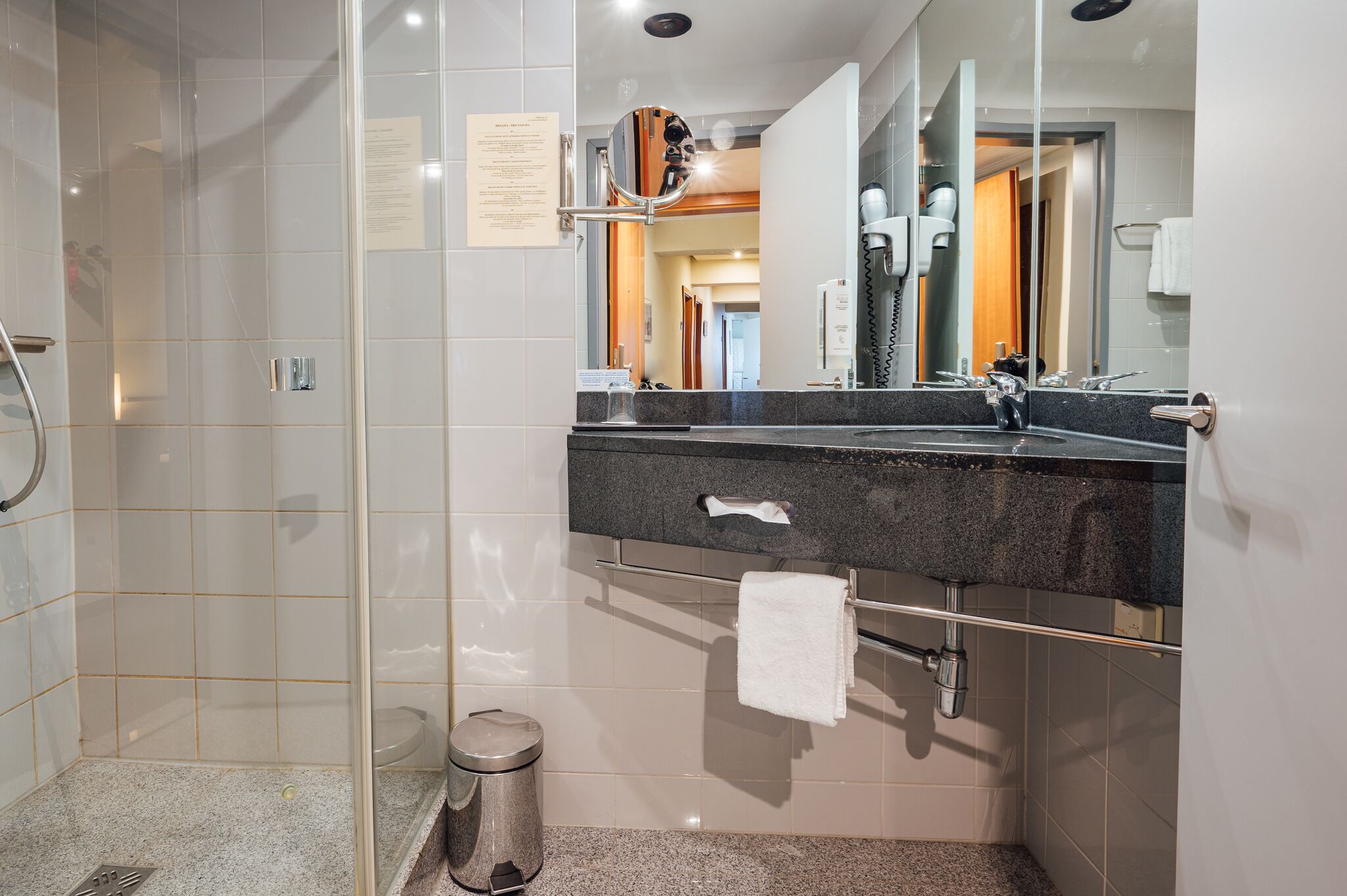 A modern bathroom with a glass shower enclosure, a granite countertop sink, a towel rack, and a mirror.