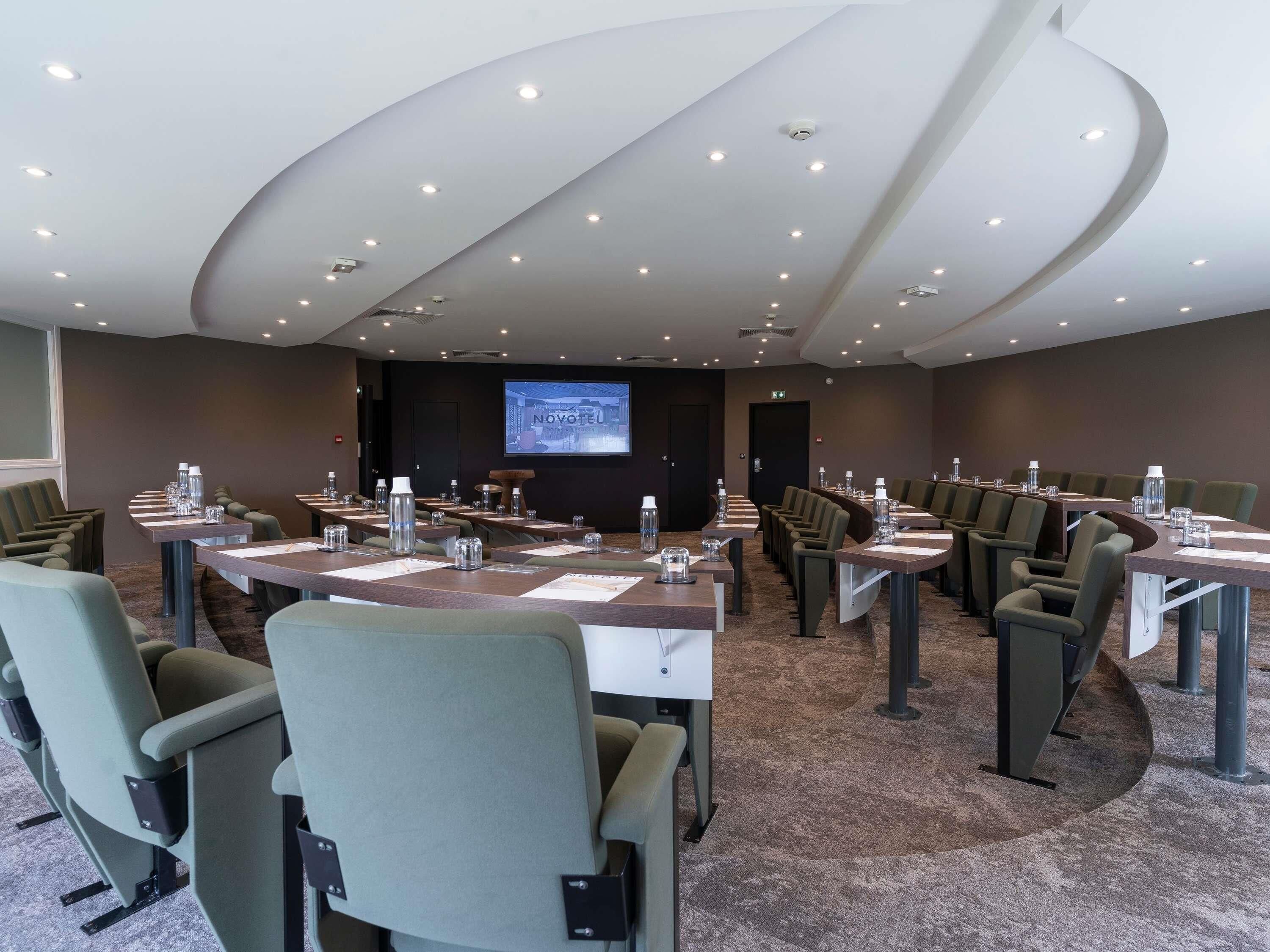 A conference room with multiple tables and chairs, a large screen, and a modern ceiling design.