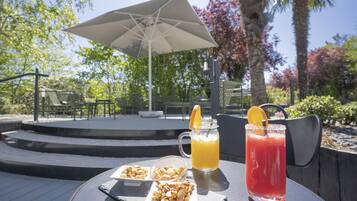 Ein Tisch mit Getränken, Nüssen und Obst, draußen mit Sonnenschirm und Stühlen im Hintergrund.