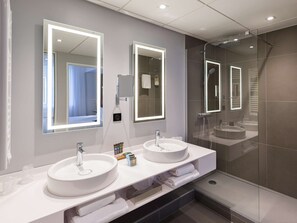 A modern bathroom with two sinks, a large mirror, and a glass shower enclosure.