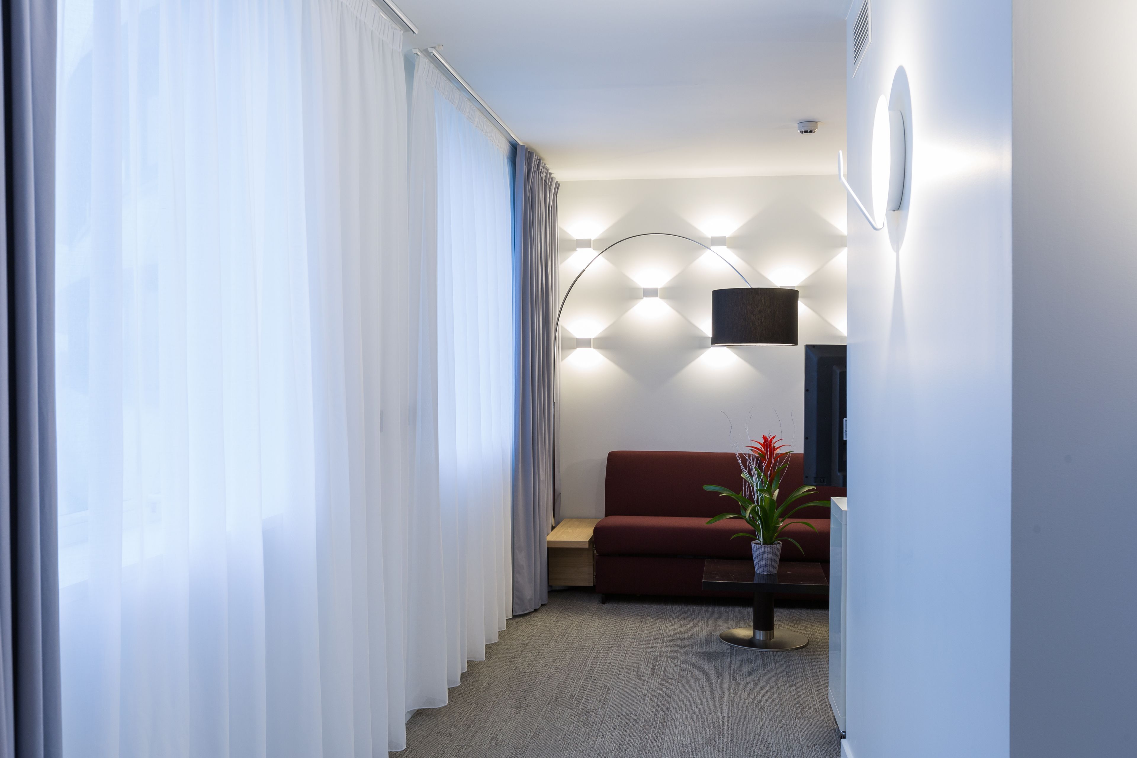 A modern living room with a red sofa, a small table with a plant, and a geometric light fixture on the wall.