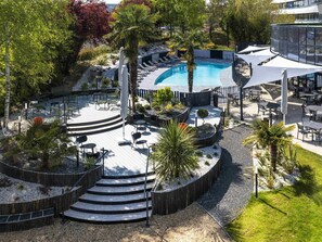 Zona de piscina con diseño circular, mobiliario exterior y una escalera que lleva a una terraza.