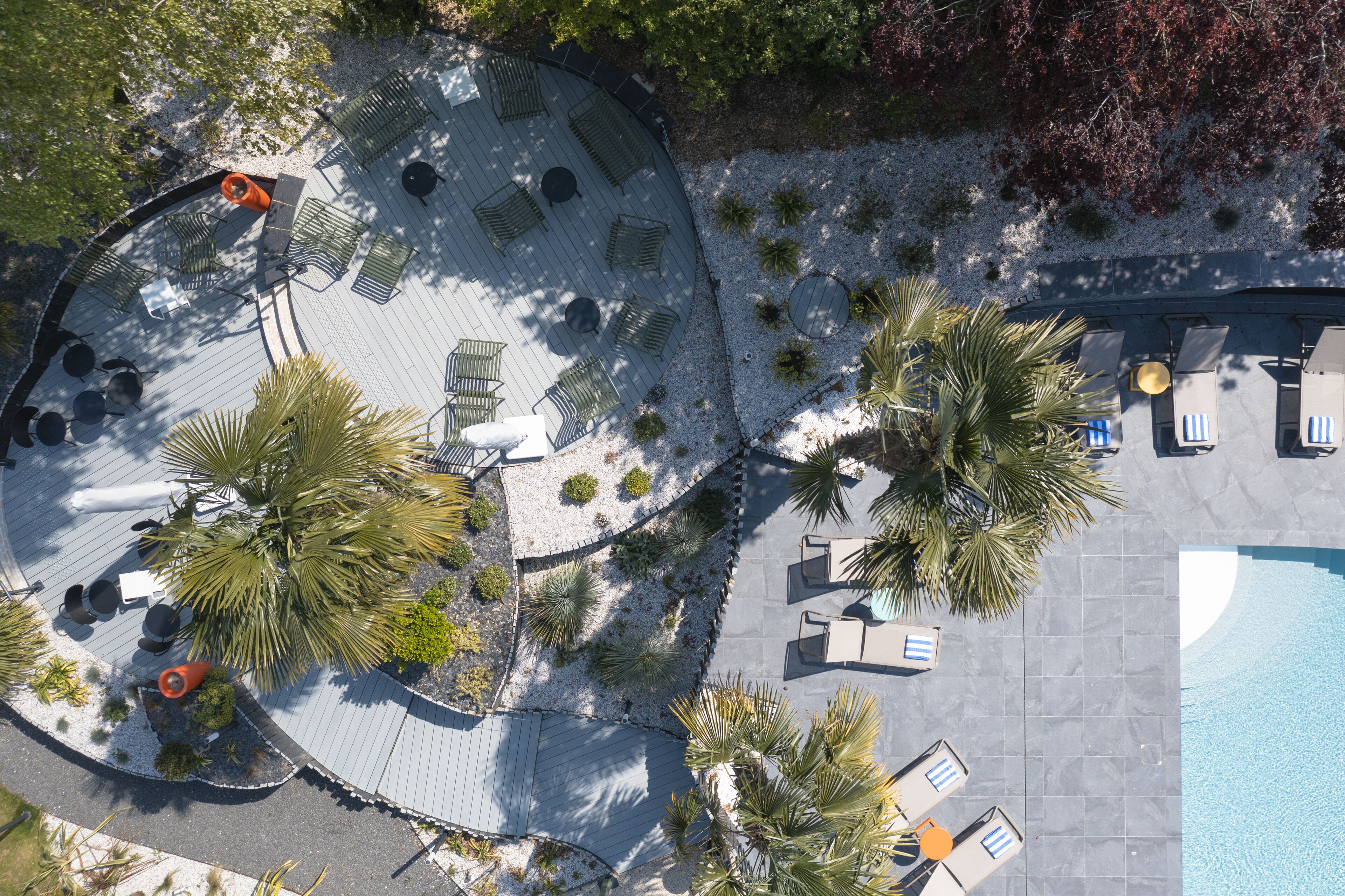 An aerial view of a resort with a pool, lounge areas, and palm trees.