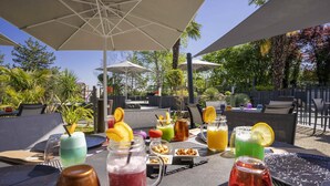 An outdoor dining area with tables, chairs, umbrellas, and various beverages.