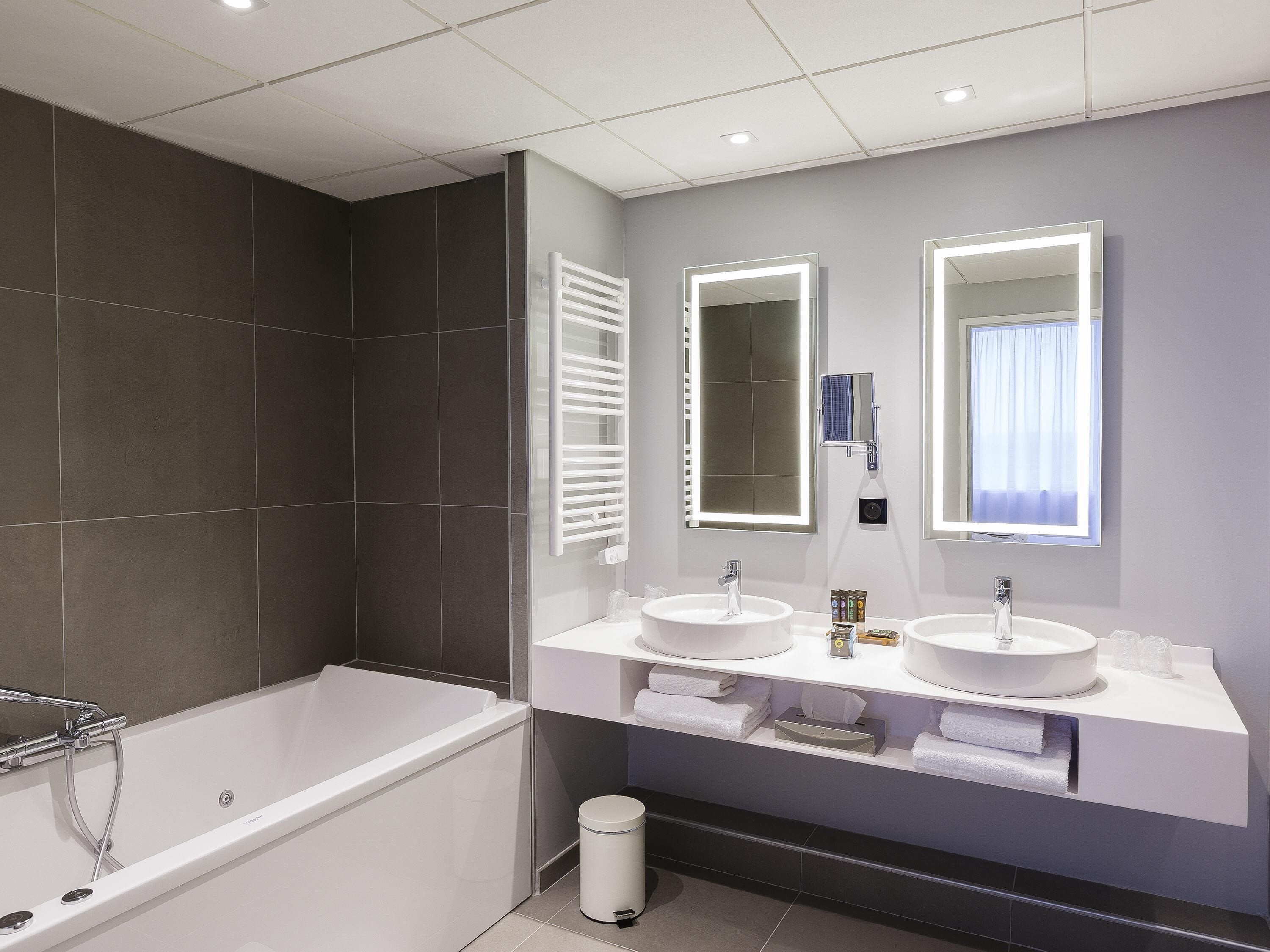 A modern bathroom with a bathtub, two sinks, and large mirrors.