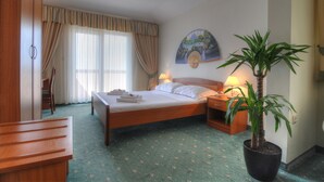 Habitación de hotel con cama, escritorio, silla, planta en maceta y un cuadro en la pared.