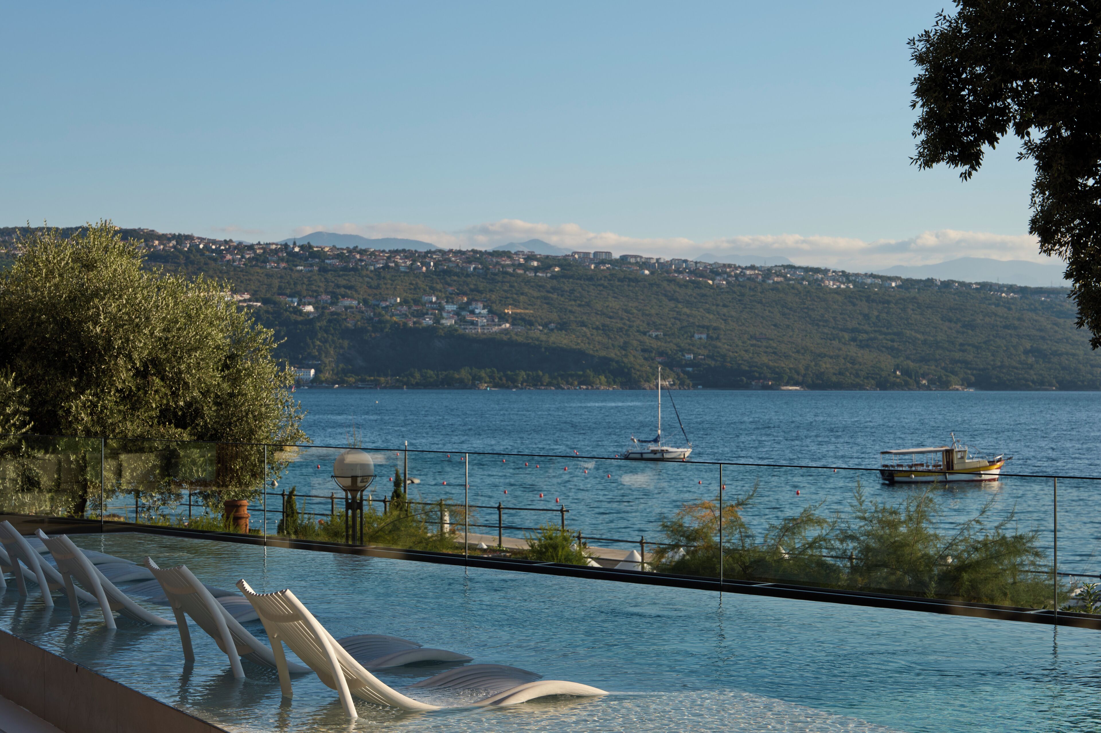 Ein Pool im Infinity-Design mit Blick auf einen See, Boote und ein fernes Bergmassiv.