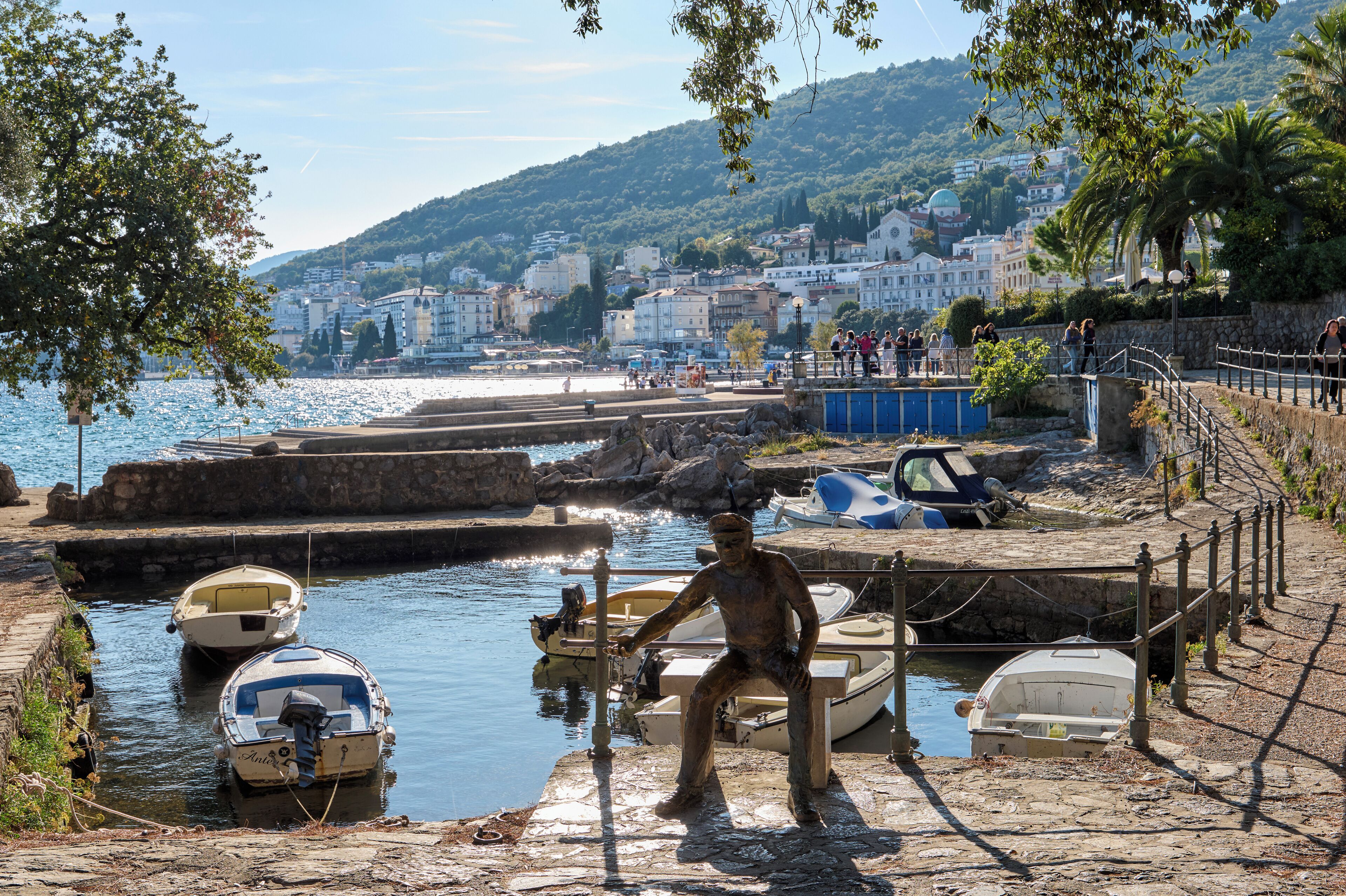 A harbor with boats docked, a statue, and buildings in the background.