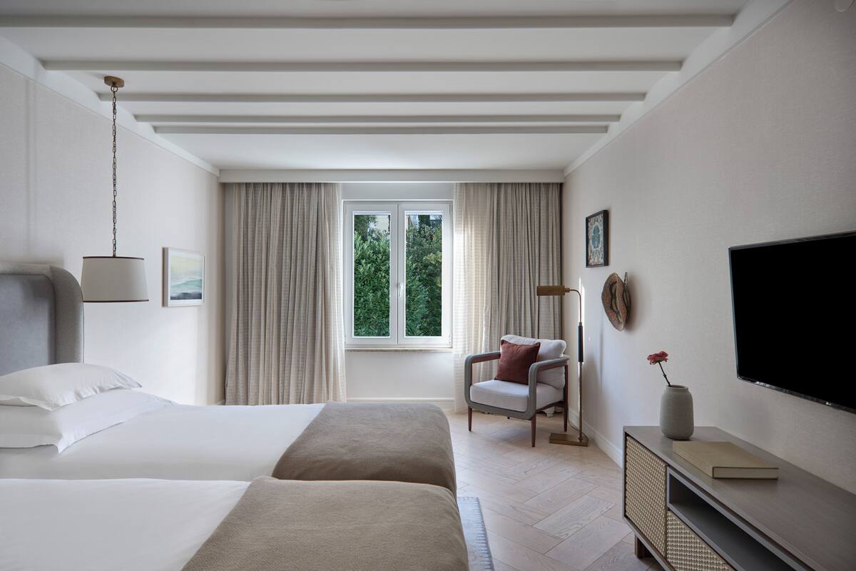 A hotel room with a bed, a chair, a TV, and a window with curtains.