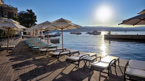 Eine Uferterrasse mit Liegestühlen und Sonnenschirmen, im Hintergrund Boote und freie Sicht auf das Wasser.