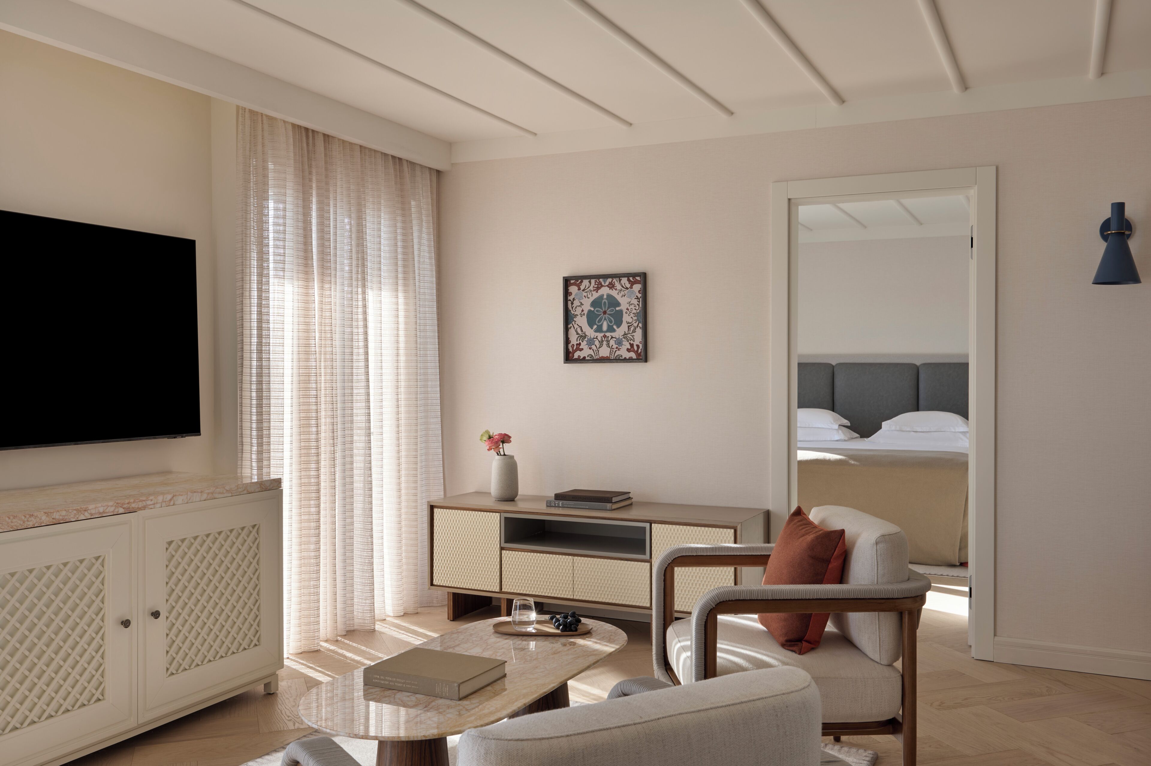 Una habitación de hotel moderna con una televisión de pantalla plana, un sofá, una mesa de centro, un armario, una mesita de noche y una cama.