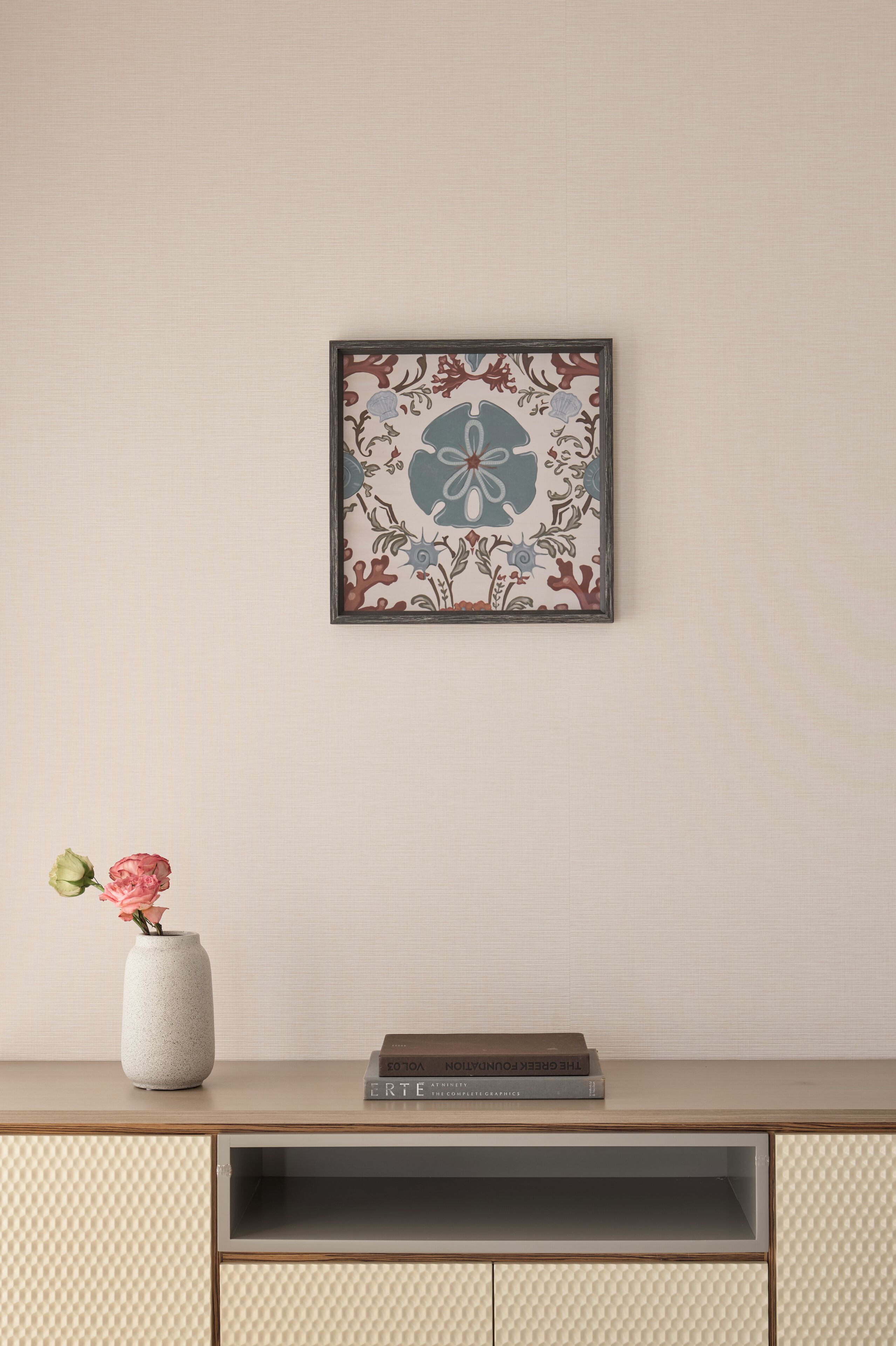 A framed artwork with a floral and nautical theme, a vase with flowers, and a book on a shelf.