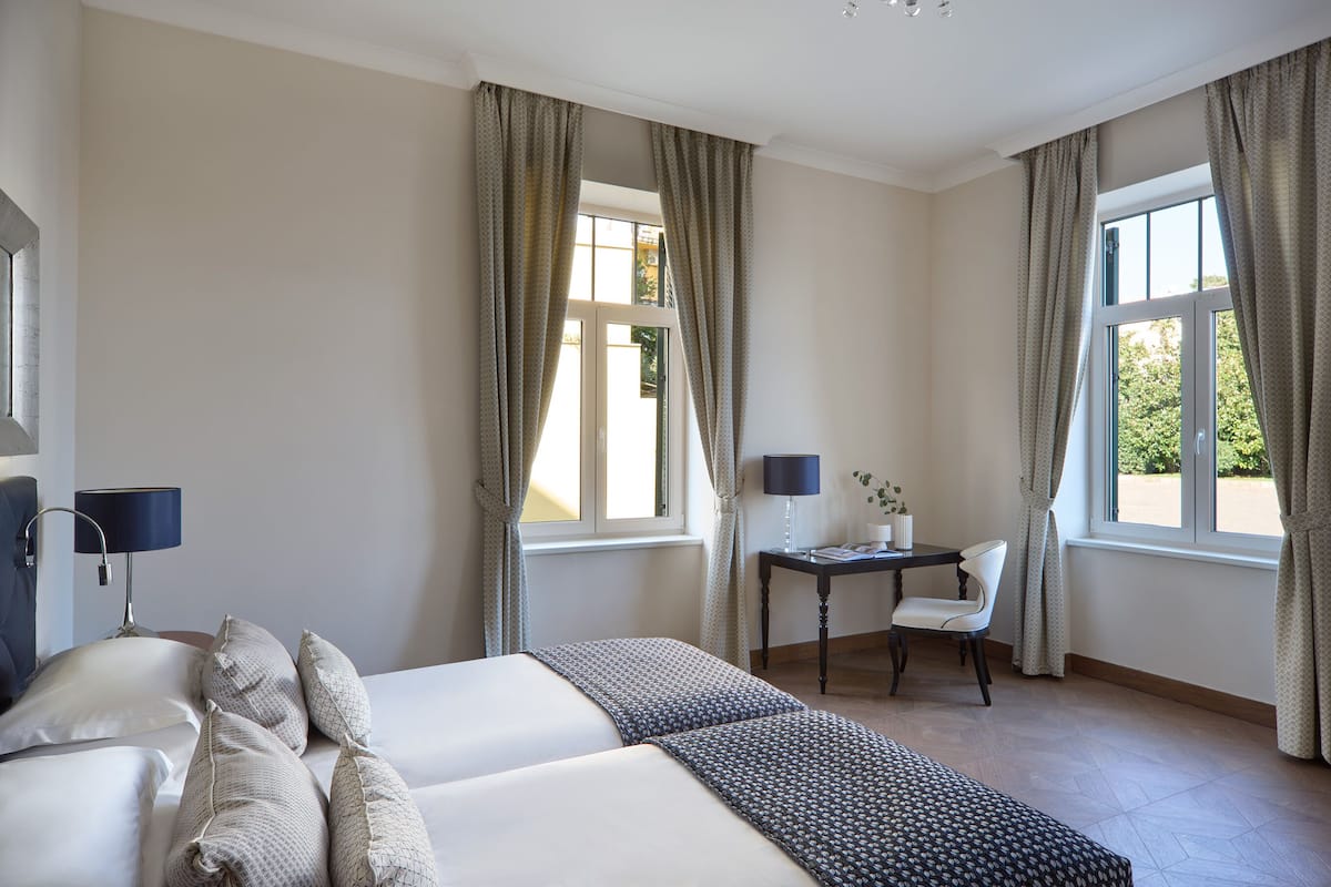 A hotel room with two beds, a desk with a chair, and a window with curtains.