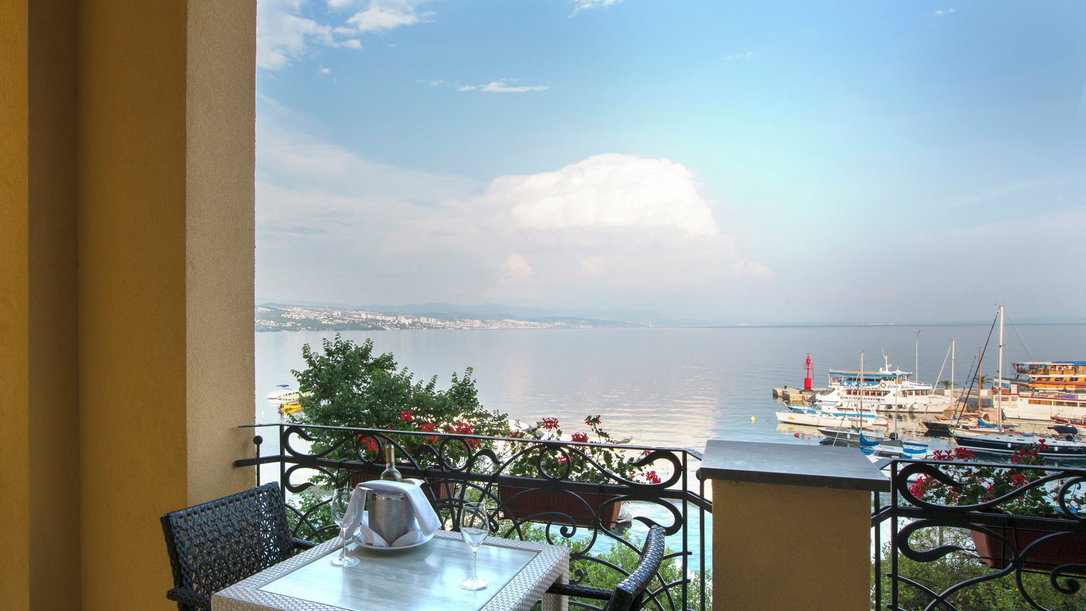 A balcony with a table and chairs, overlooking a marina with boats and a distant cityscape.