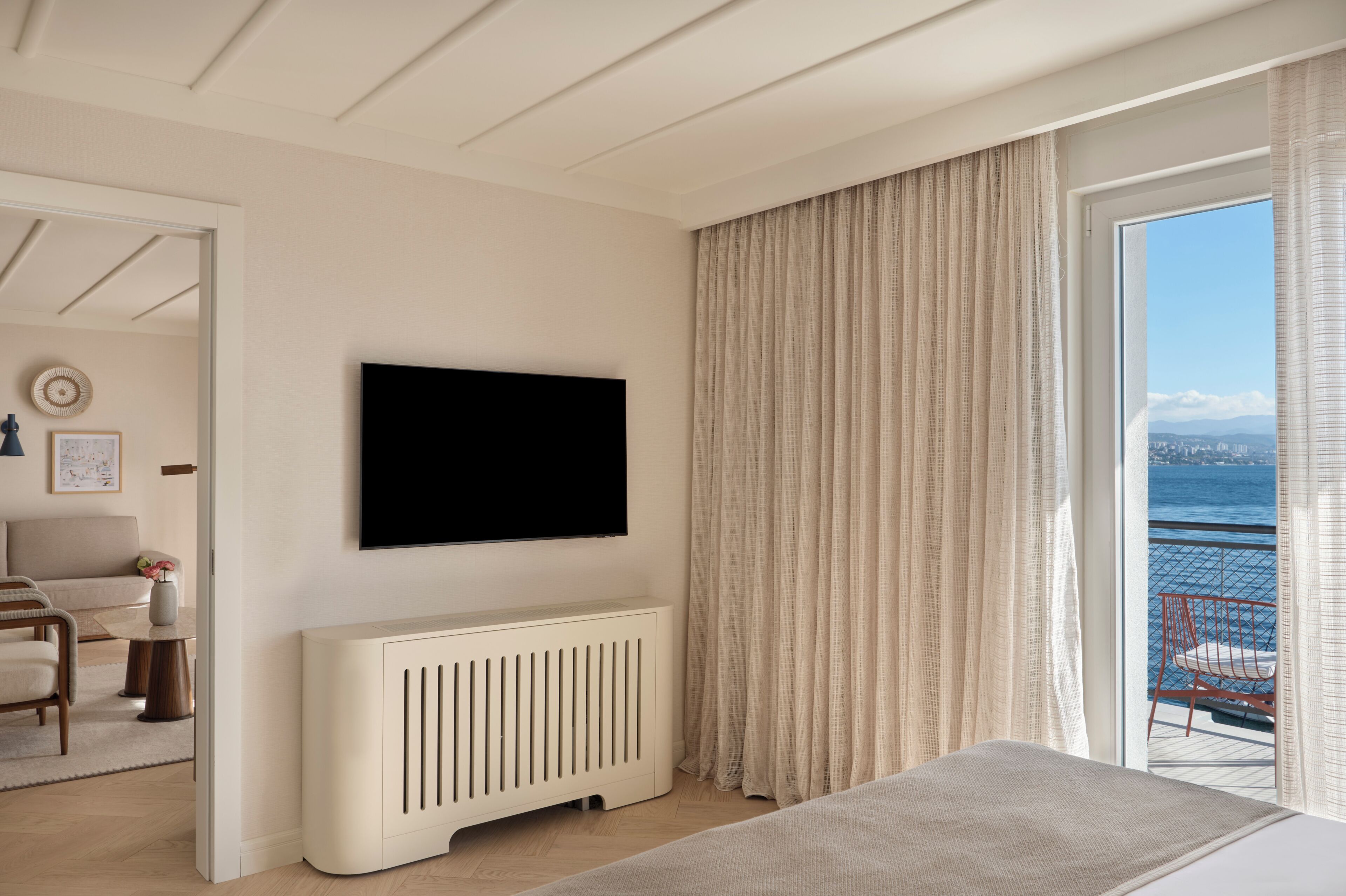 Una habitación de hotel moderna con un televisor grande, un balcón con vistas al mar y un rincón de descanso acogedor.