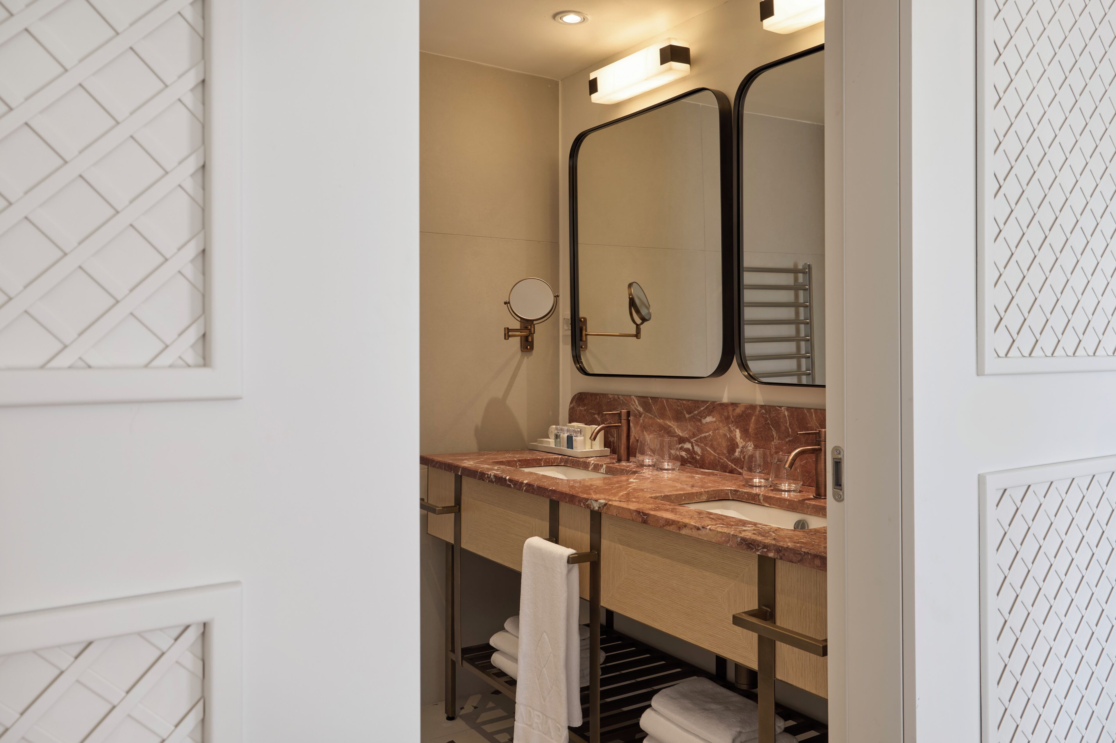 A modern bathroom with a marble sink, a large mirror, and a towel rack.
