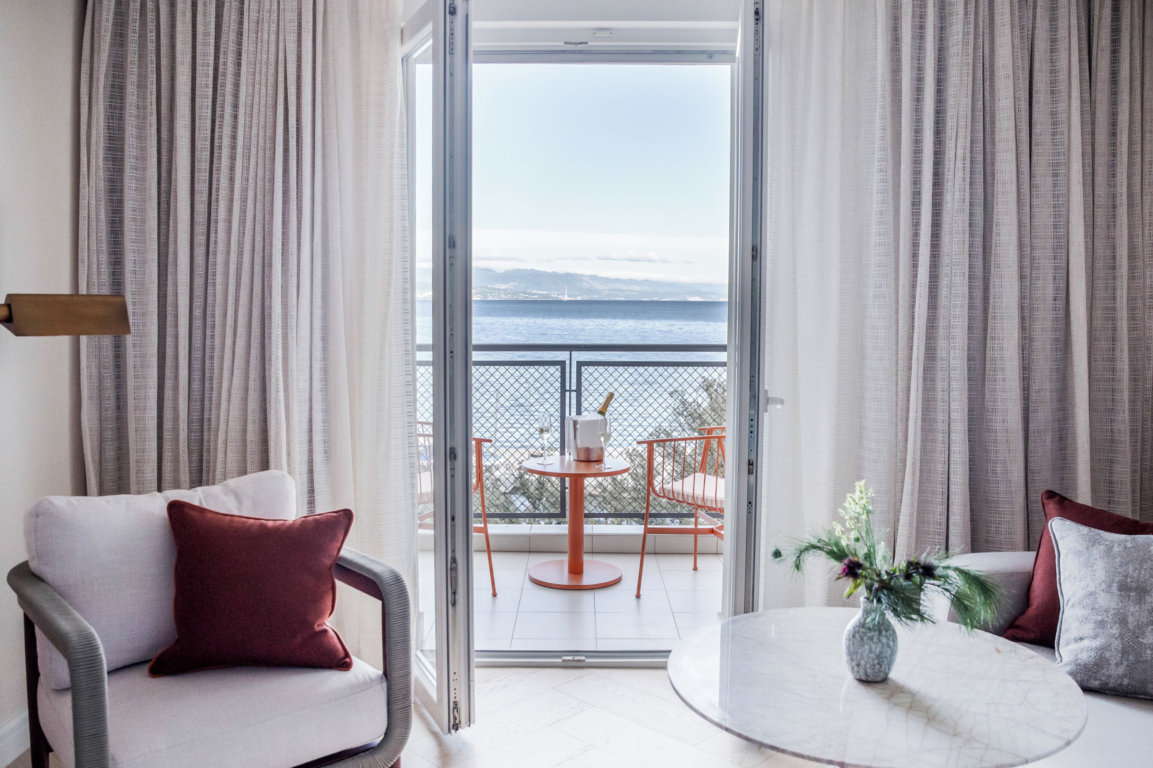 A room with a balcony, a white sofa, a round table, and a vase with flowers.