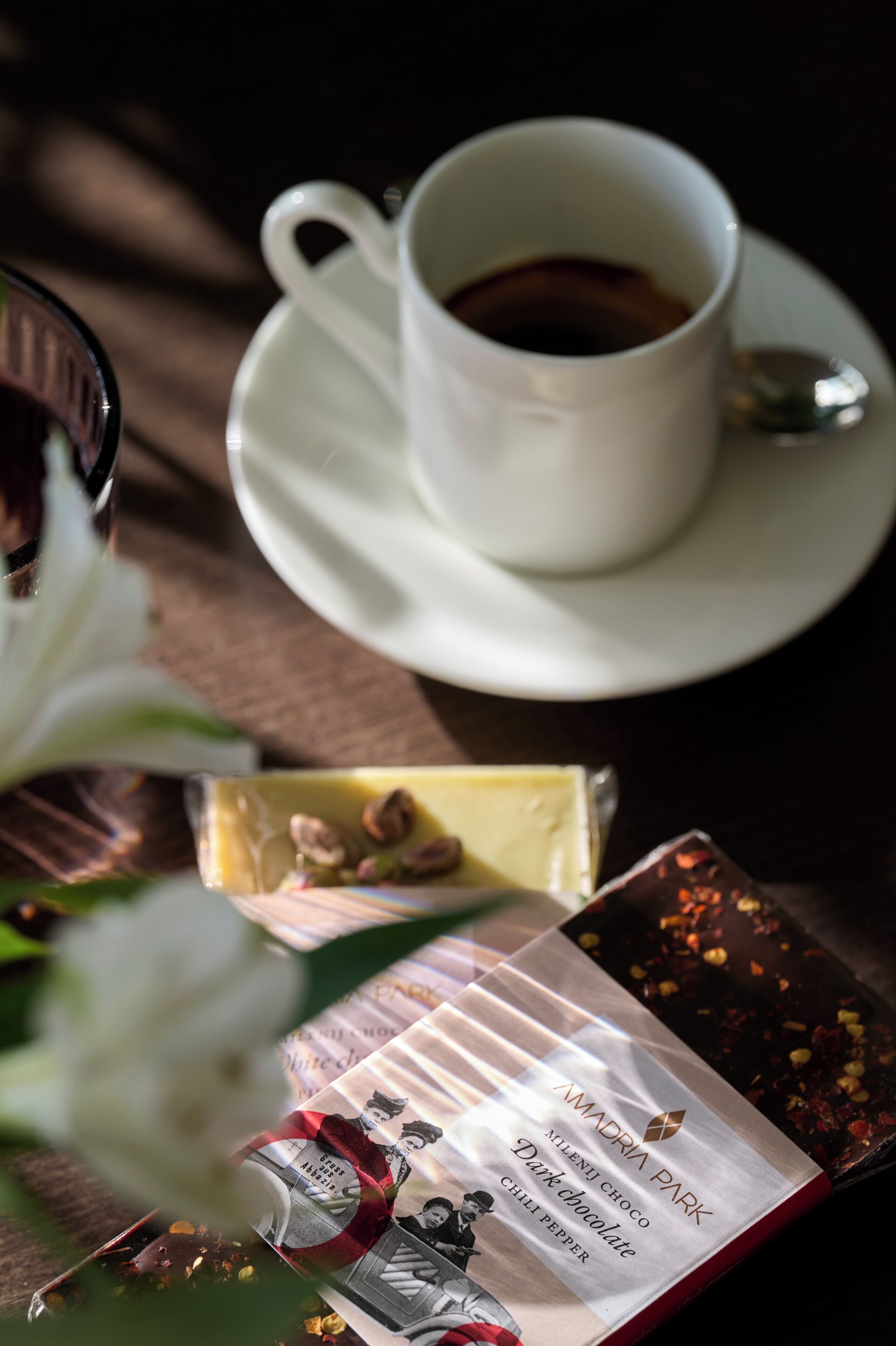 Een kop koffie op een schotel met een lepel, een chocoladereep en een chocoladeverpakking op een tafel.