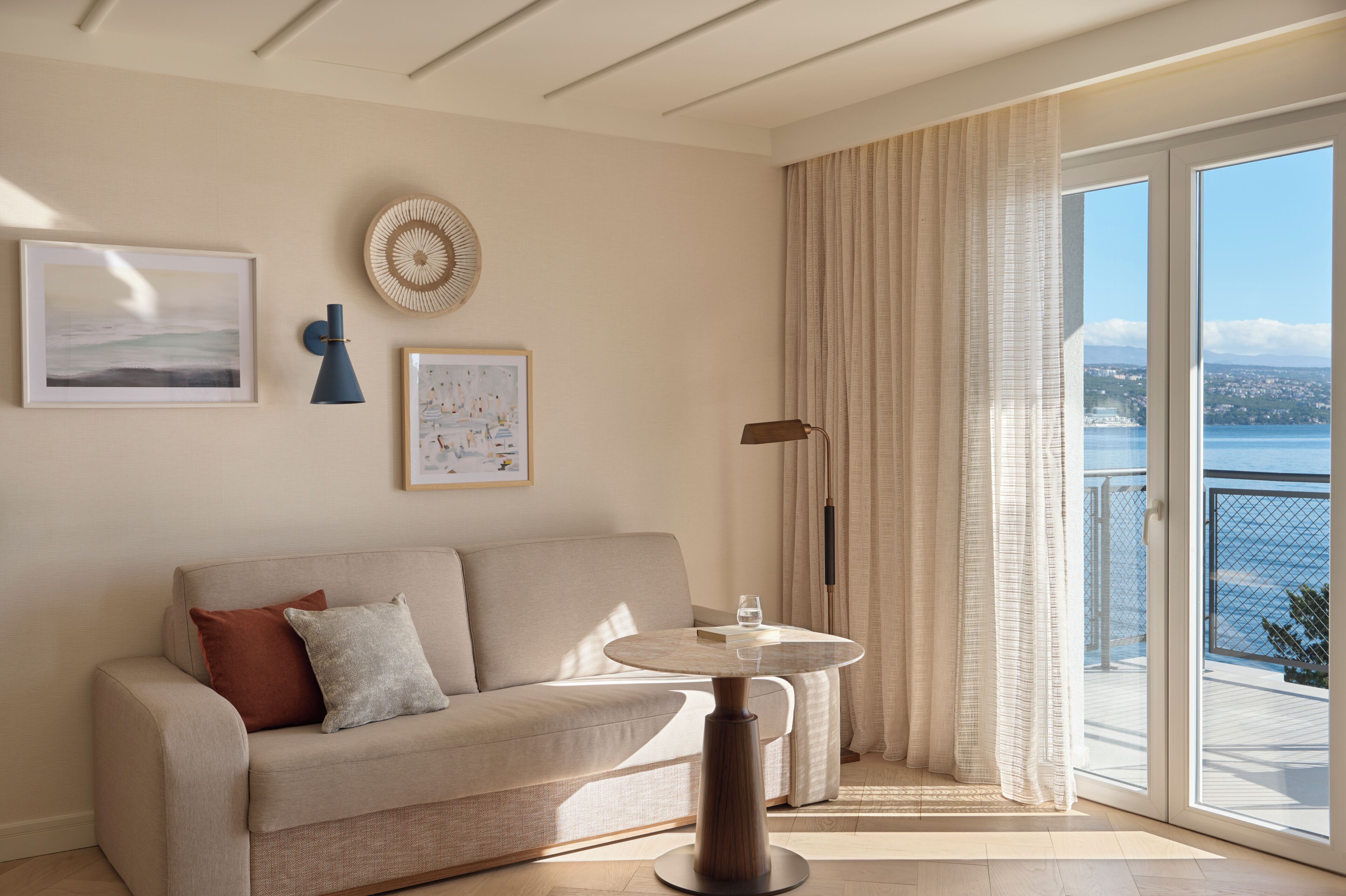 Ein modernes Wohnzimmer mit einer Couch, einem runden Tisch und Meerblick durch große Fenster.