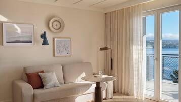 A modern living room with a sofa, a round table, and a view of the sea through large windows.