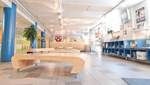 A spacious lobby with a central wooden bench, a reception desk, and a wall with informational posters. - Eurohostel (Helsinki)