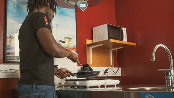 A person cooking on a stove in a red-walled kitchen with a microwave and a sink.