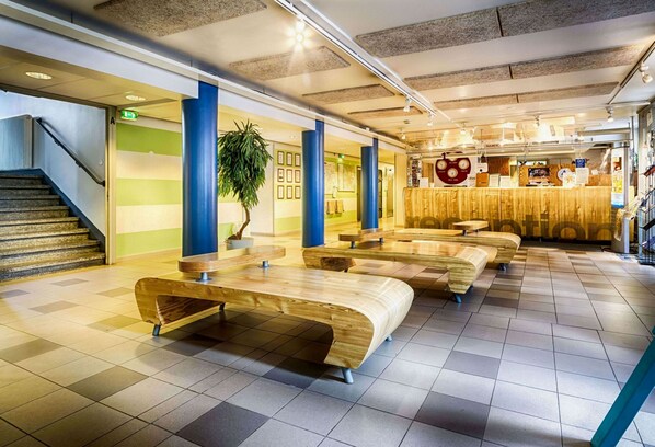 A modern interior with a staircase, wooden benches, a reception area, and a green wall with framed pictures. - Eurohostel (Helsinki)