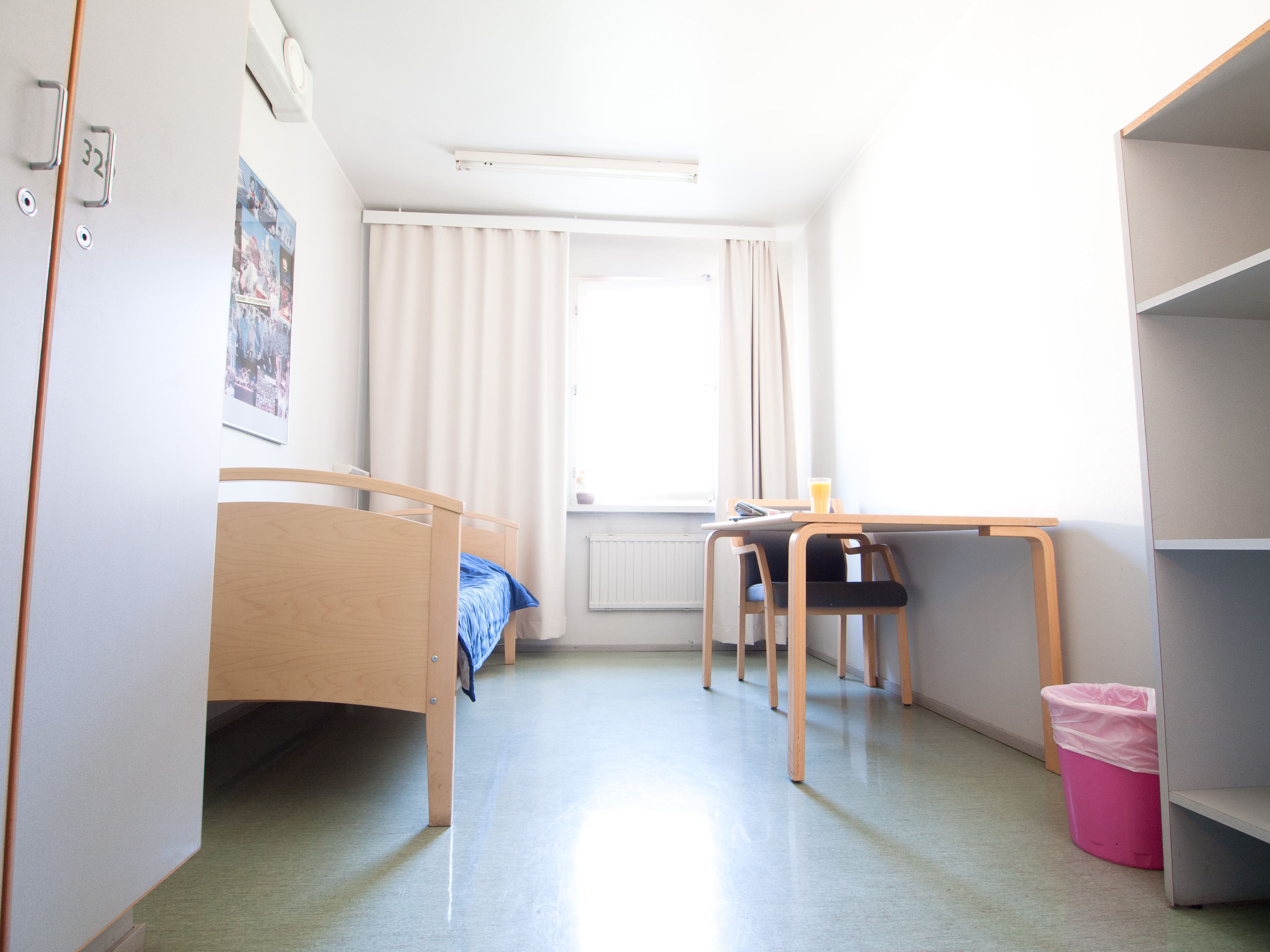 A small, bright room with a bed, a desk, and a chair.