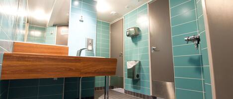 A modern bathroom with teal tiles, a wooden bench, a hand dryer, and a urinal.