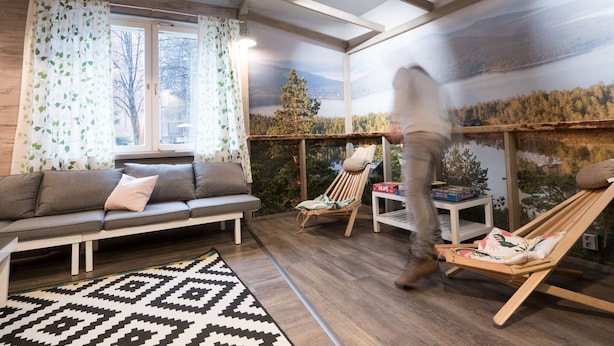 A cozy room with a wooden ceiling, a sofa, a chair, and a large window with a view of a lake and forest. - Eurohostel (Helsinki)