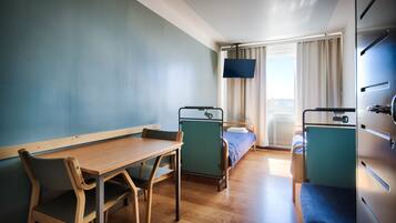 Una habitación con escritorio de madera, dos sillas, una cama, un televisor y una ventana con cortinas.