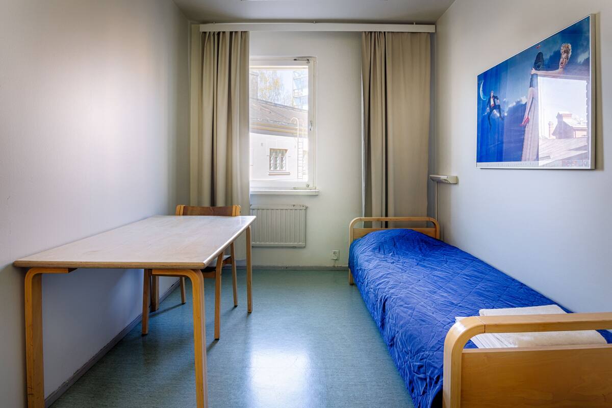 A room with a single bed, a wooden table, and a window with curtains.