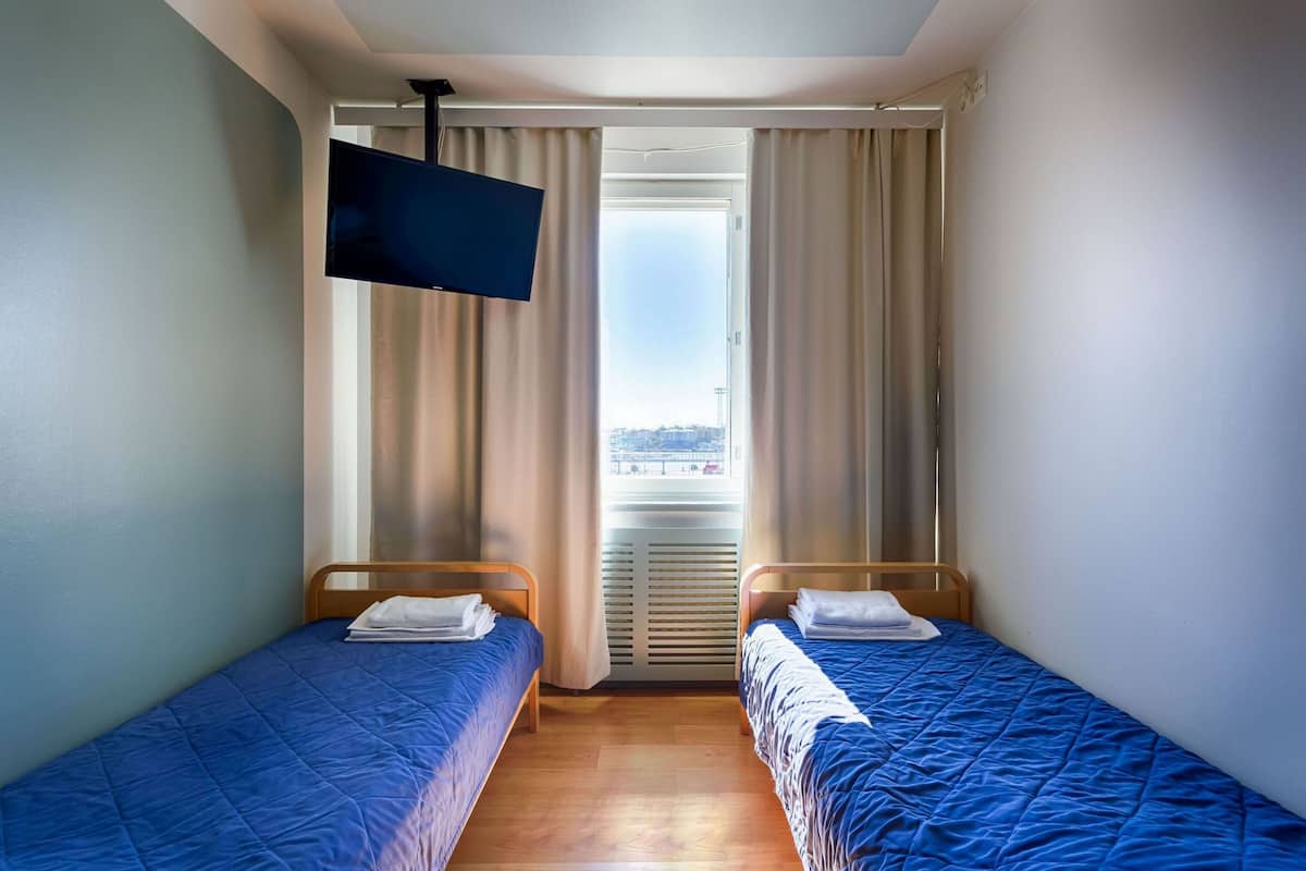 A hotel room with two single beds, a flat-screen TV, and a large window with curtains.