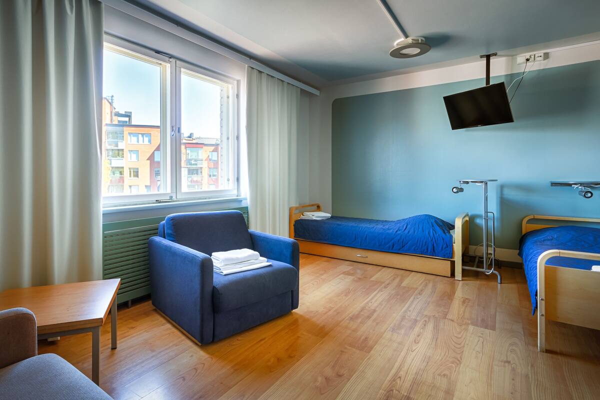 A hotel room with a bed, a chair, a desk, a TV, and a window with curtains.